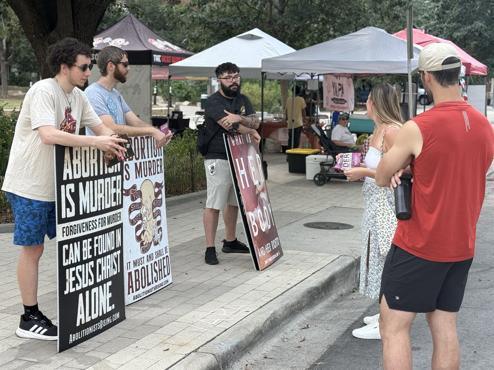 Abolitionists speaking with passersby beside signs at an outdoor market