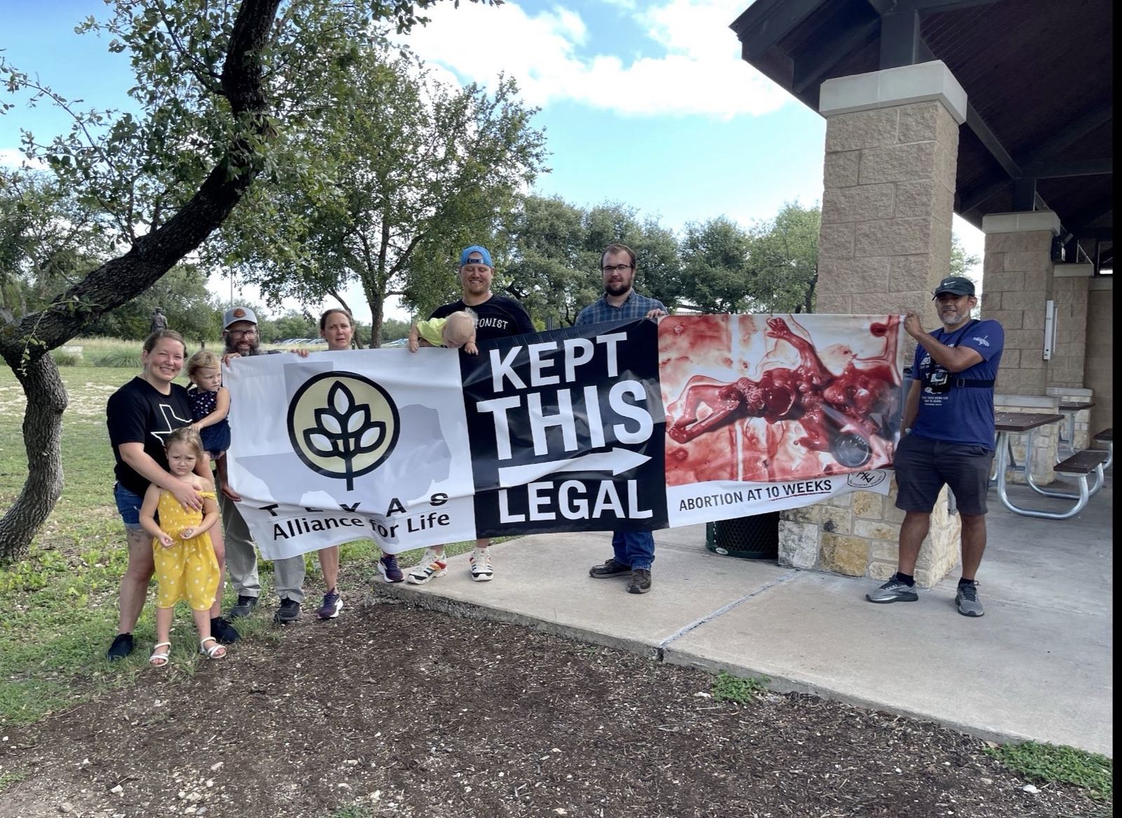 A group holding the same banner under a park pavilion