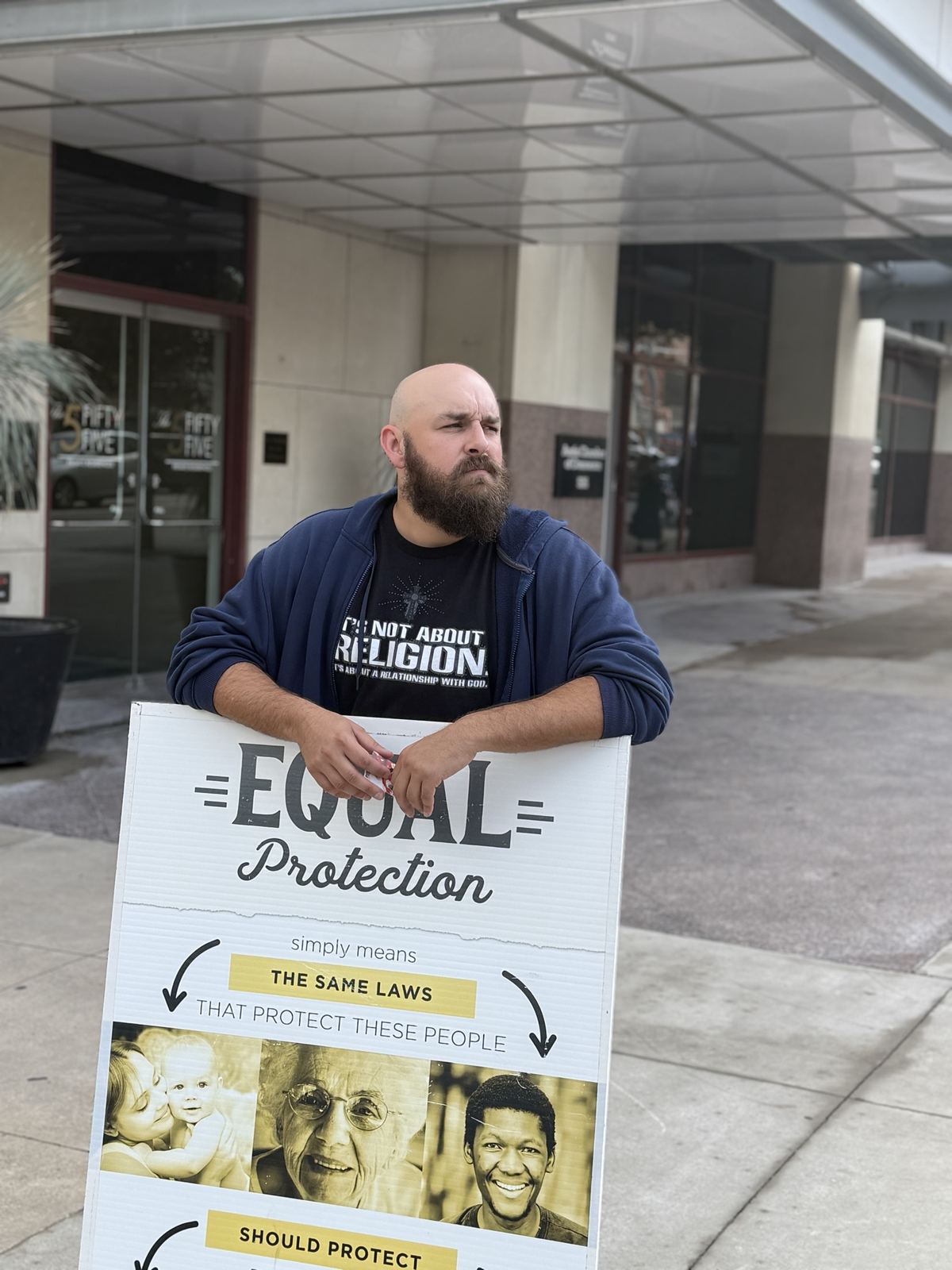 A man with an equal protection sign outside a building